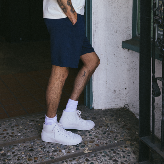A person wearing white high-top Red Ball Jets sneakers and navy shorts stands near a doorway on a textured stone floor.