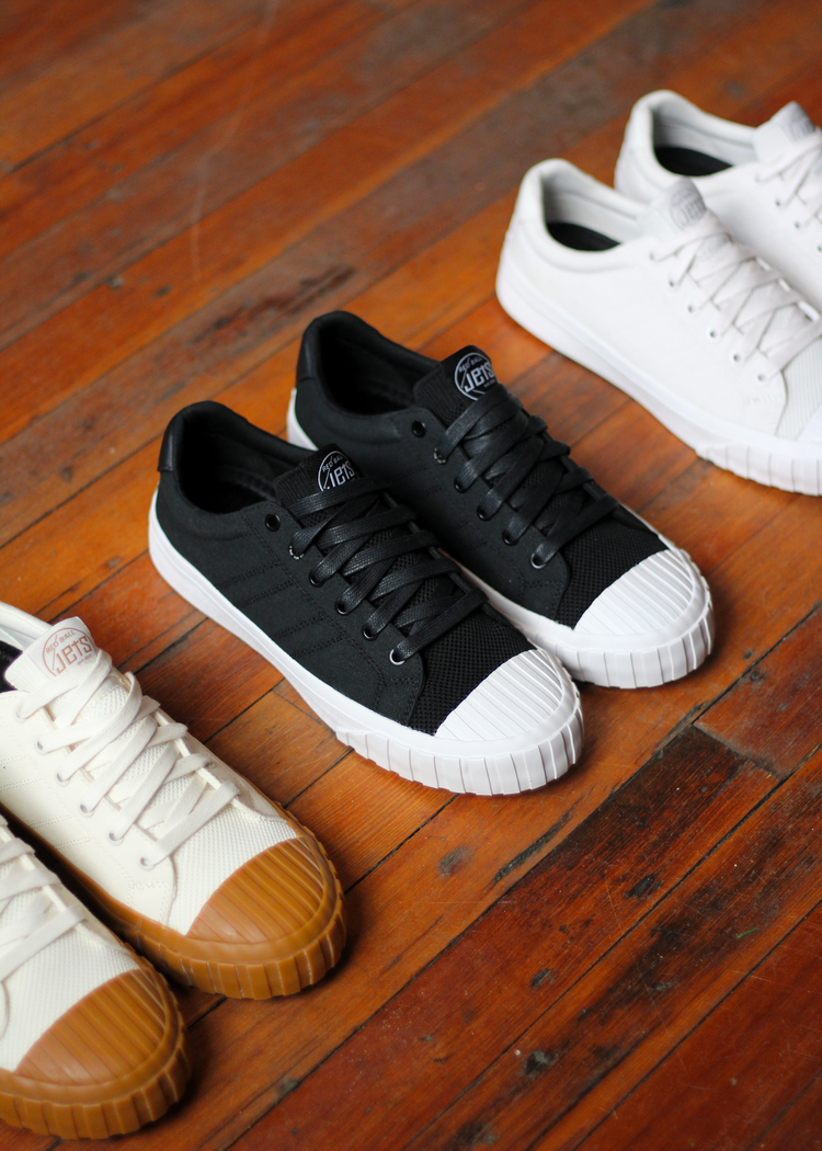 Three Red Ball Jets Legacy Collection low-top sneakers arranged on a warm wooden floor — Off-White Legacy LO with gum sole in the foreground left, Black Legacy LO centered, and White Legacy LO partially visible in the upper right.