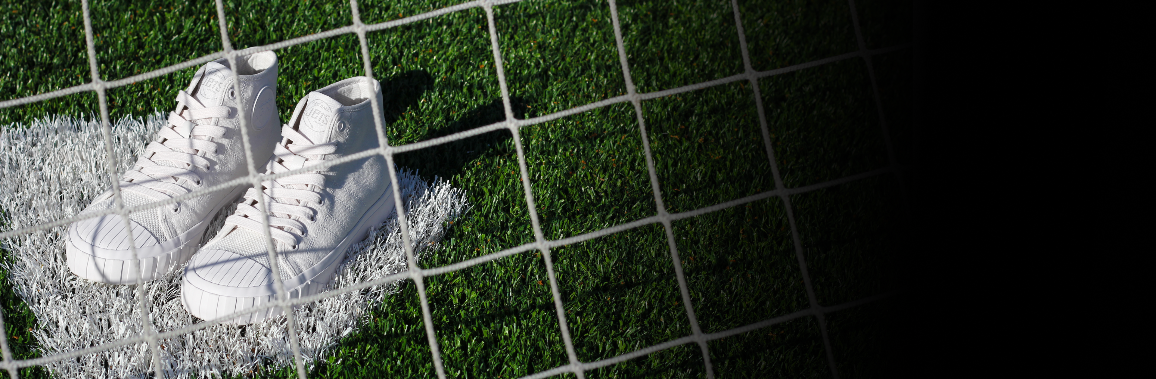 White sneakers on a grassy surface with a wire mesh background