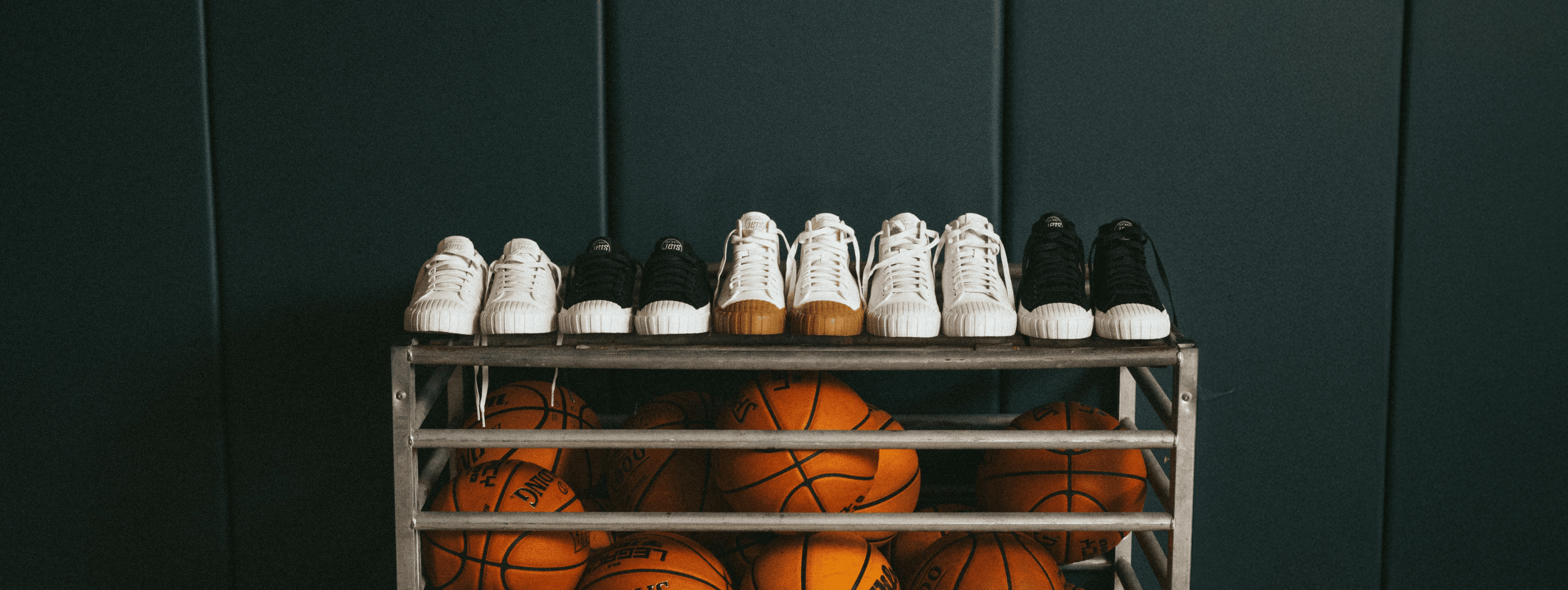 Basketballs and shoes on a metal rack against a dark green wall.