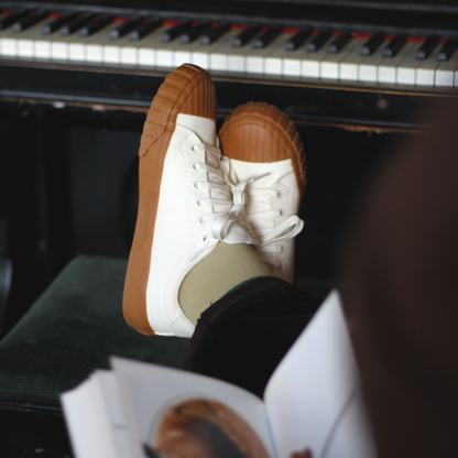 Gum-sole shoes with white laces on a piano bench.