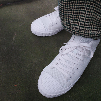 White sneakers worn with checkered pants on a concrete floor