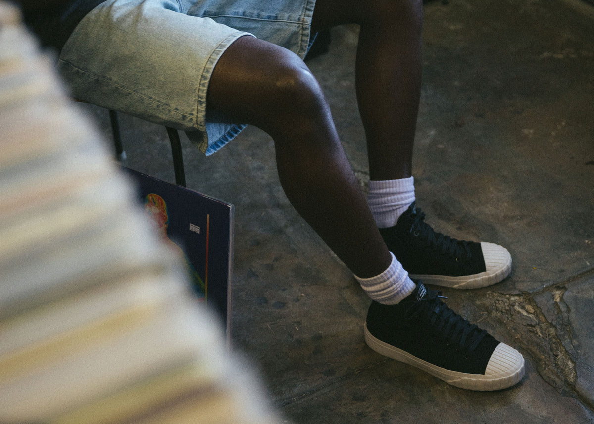 Red Ball Jets' black low-tops on a black model sitting in a record shop