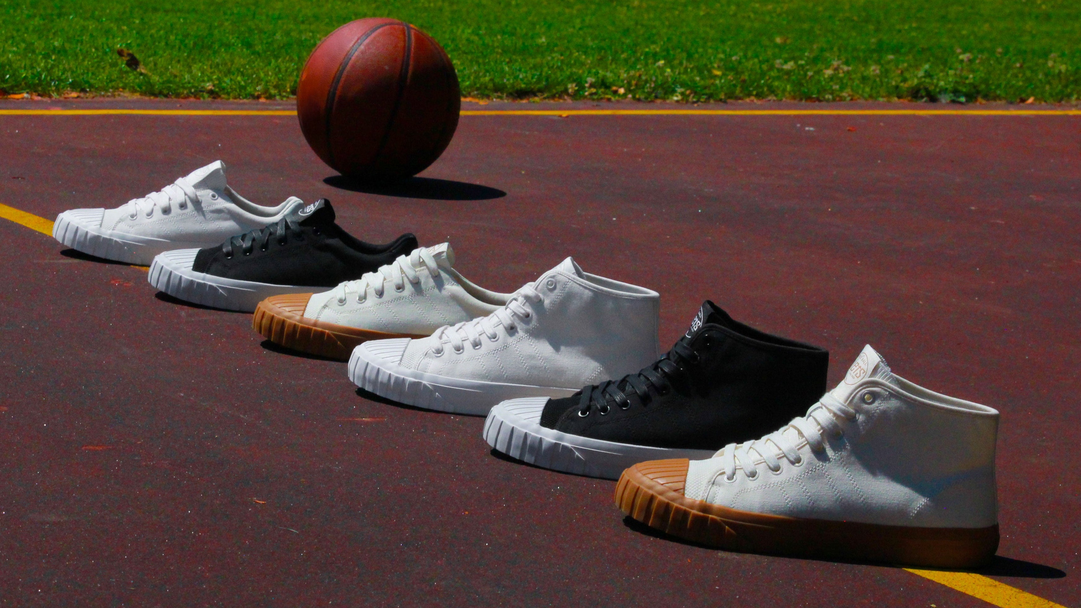 Six sneakers in white and black are lined up on a red basketball court with a basketball in the background.