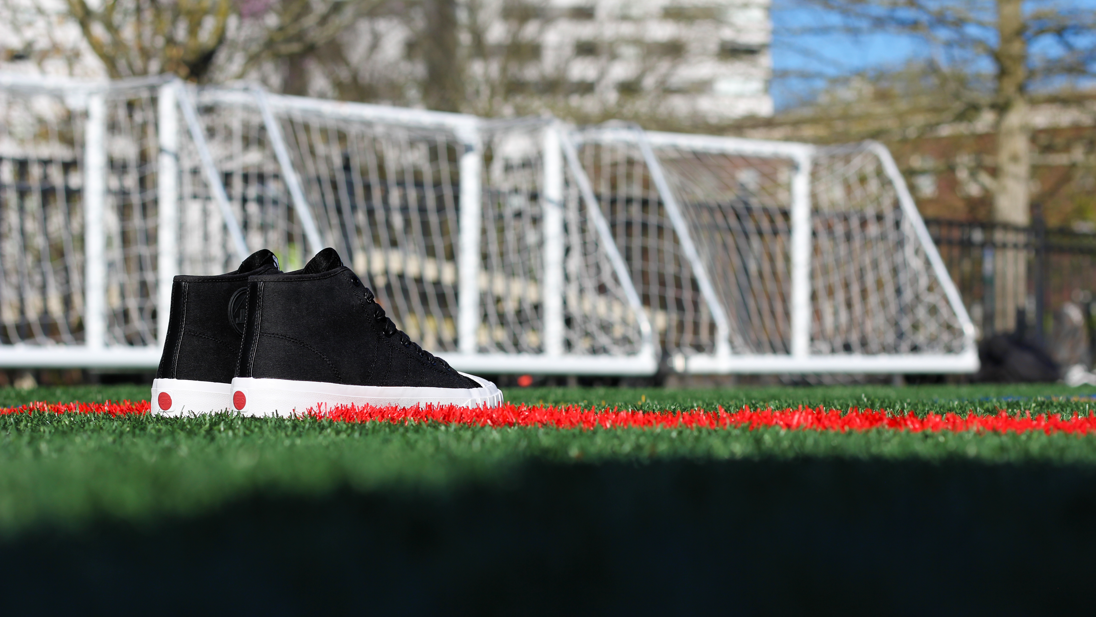 Black sneaker on artificial grass with a soccer goal in the background